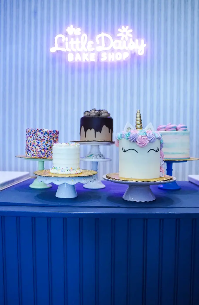 Little Daisy neon sign glowing above a display of cakes